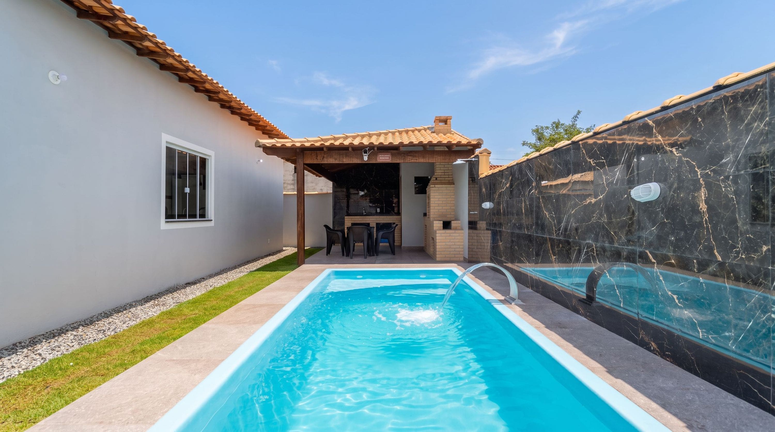 Una piscina con un patio, una zona de estar cubierta y un muro de piedra.