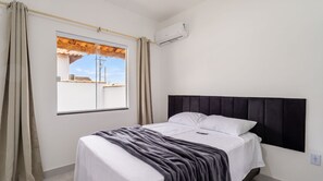 Ett hotellrum med en säng, ett fönster med gardiner, en luftkonditioneringsanläggning och utsikt över byggnader utanför.
