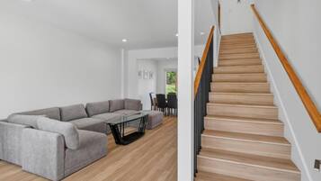 A modern living room with a grey sectional sofa, a glass coffee table, and a wooden staircase with a wooden handrail.