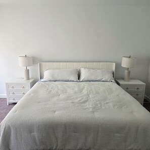 Een bed met een wit hoofdeinde en twee nachtkastjes met lampen.
