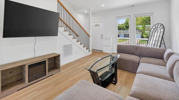 A modern living room with a flat-screen TV, wooden flooring, a staircase, a sofa, and a glass coffee table. - New 3bdrHome • 2 Min to Downtown.2.5 bathroom (Spartanburg)