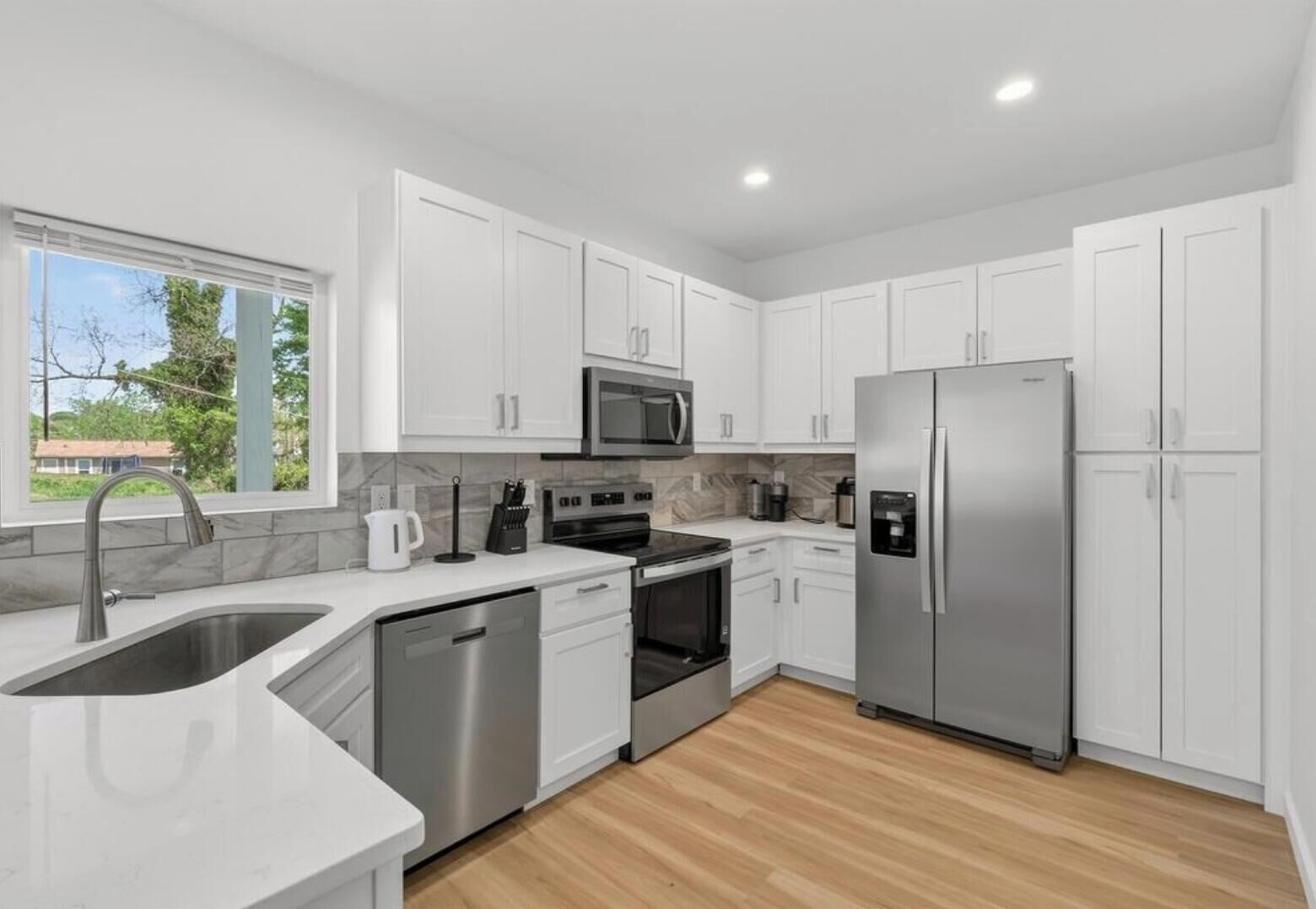 Una cocina moderna con armarios blancos, electrodomésticos de acero inoxidable y piso de madera.