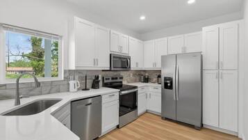 Una cocina moderna con armarios blancos, electrodomésticos de acero inoxidable y piso de madera.