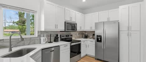 Una cocina moderna con armarios blancos, electrodomésticos de acero inoxidable y piso de madera.