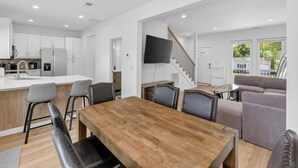 A modern kitchen with white cabinets, a wooden dining table, and bar stools. - New 3bdrHome • 2 Min to Downtown.2.5 bathroom (Spartanburg)