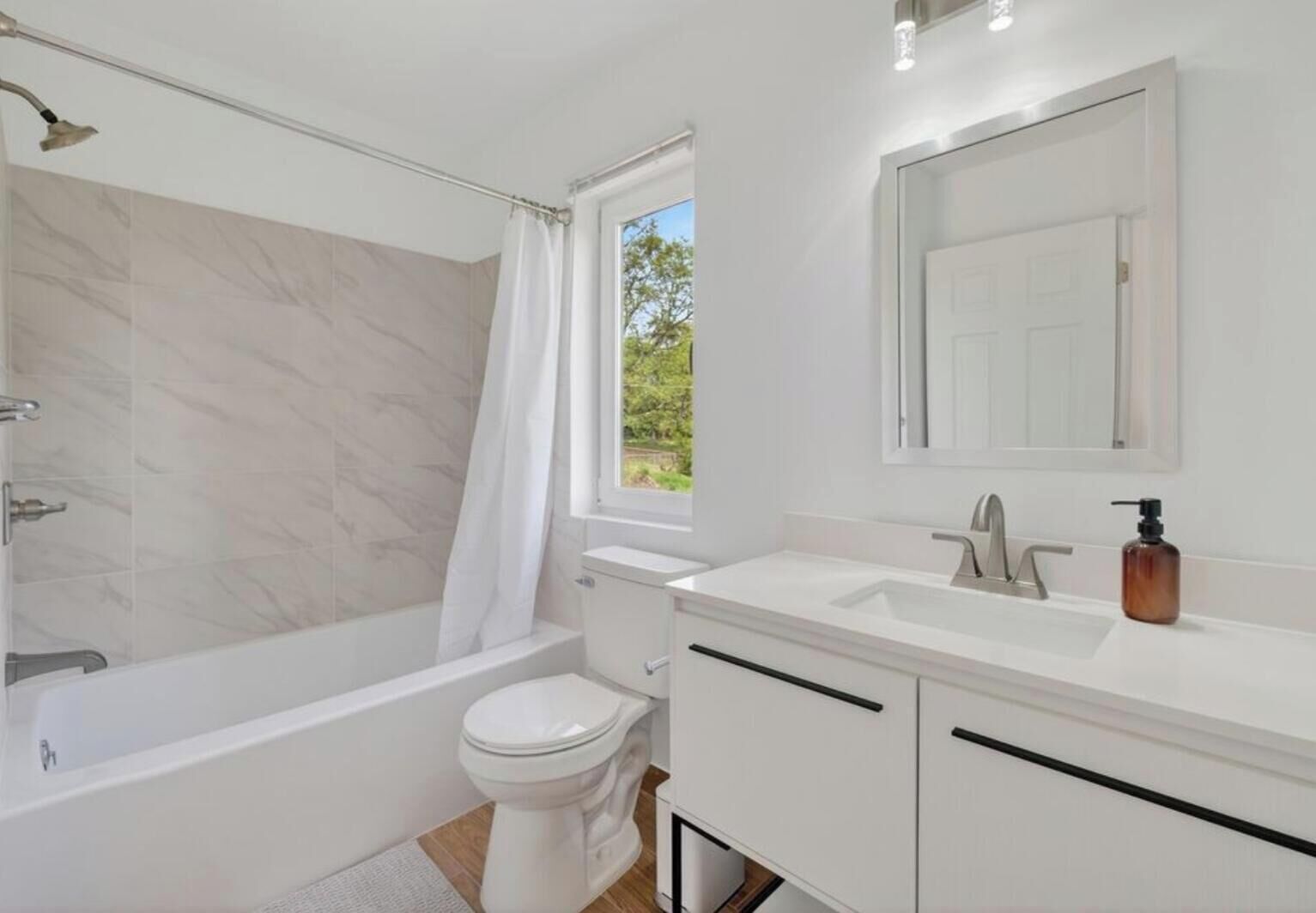 A modern bathroom with a bathtub, toilet, and vanity with a mirror.