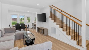 A modern living room with a staircase, a flat-screen TV, and a dining area with chairs and a table. - New 3bdrHome • 2 Min to Downtown.2.5 bathroom (Spartanburg)