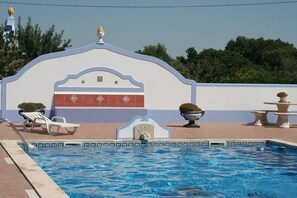 A swimming pool with a tiled edge, a white building with a decorative arch, and a fountain. - Country House 'Casa Da Quinta' with Shared Pool and Shared Garden (Évora)