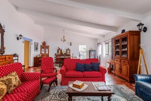 A spacious living room with a red patterned sofa, a wooden cabinet, and a dining area with a table and chairs. - Country House 'Casa Da Quinta' with Shared Pool and Shared Garden (Évora)