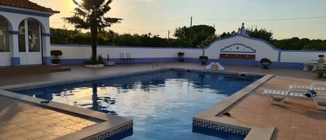 Una piscina con un borde empinado de baldosas, una palmera y un edificio con fachada azul y blanca.