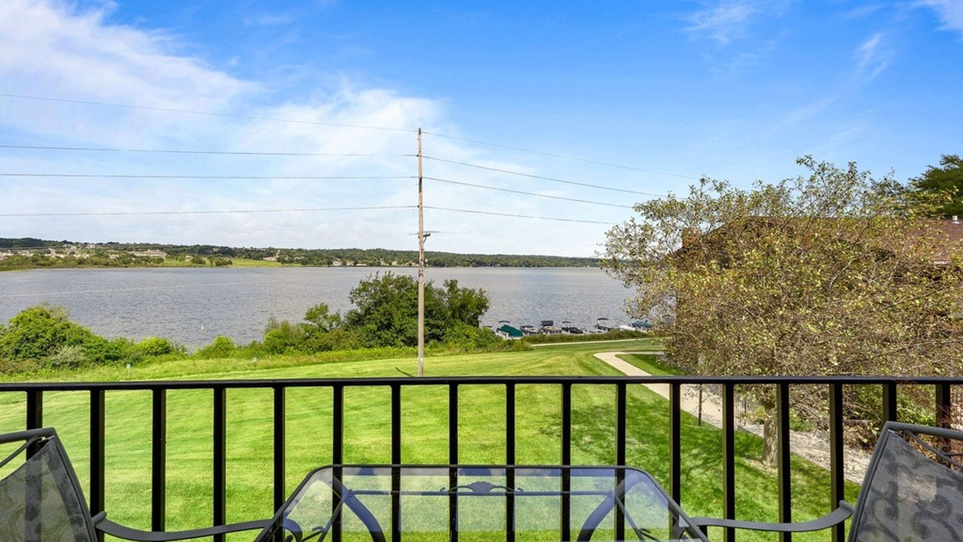 A balcony with a view of a lake, a grassy area, and a distant shoreline.