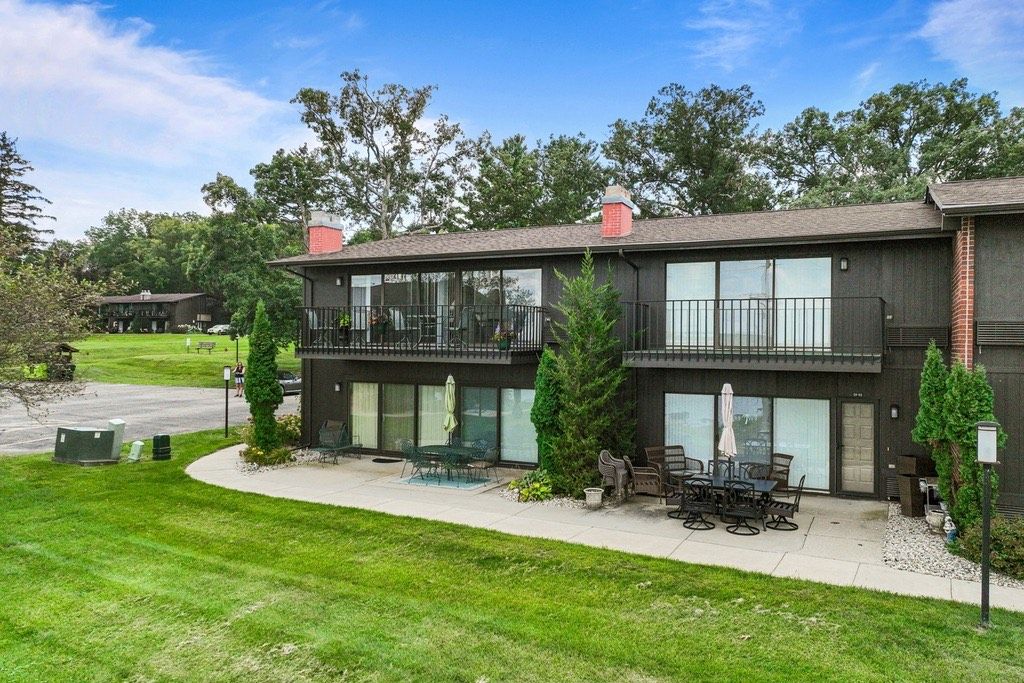 A modern two-story building with a balcony, outdoor seating area, and a well-maintained lawn.