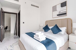 Ein Hotelzimmer mit einem Bett, einem Nachttisch, einer Lampe, einem Gemälde und einer Tür zu einem anderen Raum.