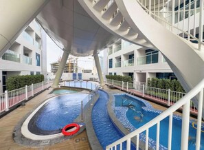 A modern building with a unique curved staircase and two swimming pools. - Luxury 2BR Dubai Retreat with Pool, Gym & Housekeeping (Dubai)