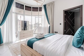 A modern bedroom with a bed, curtains, a dresser, and a view of the city. - Luxury 2BR Dubai Retreat with Pool, Gym & Housekeeping (Dubai)