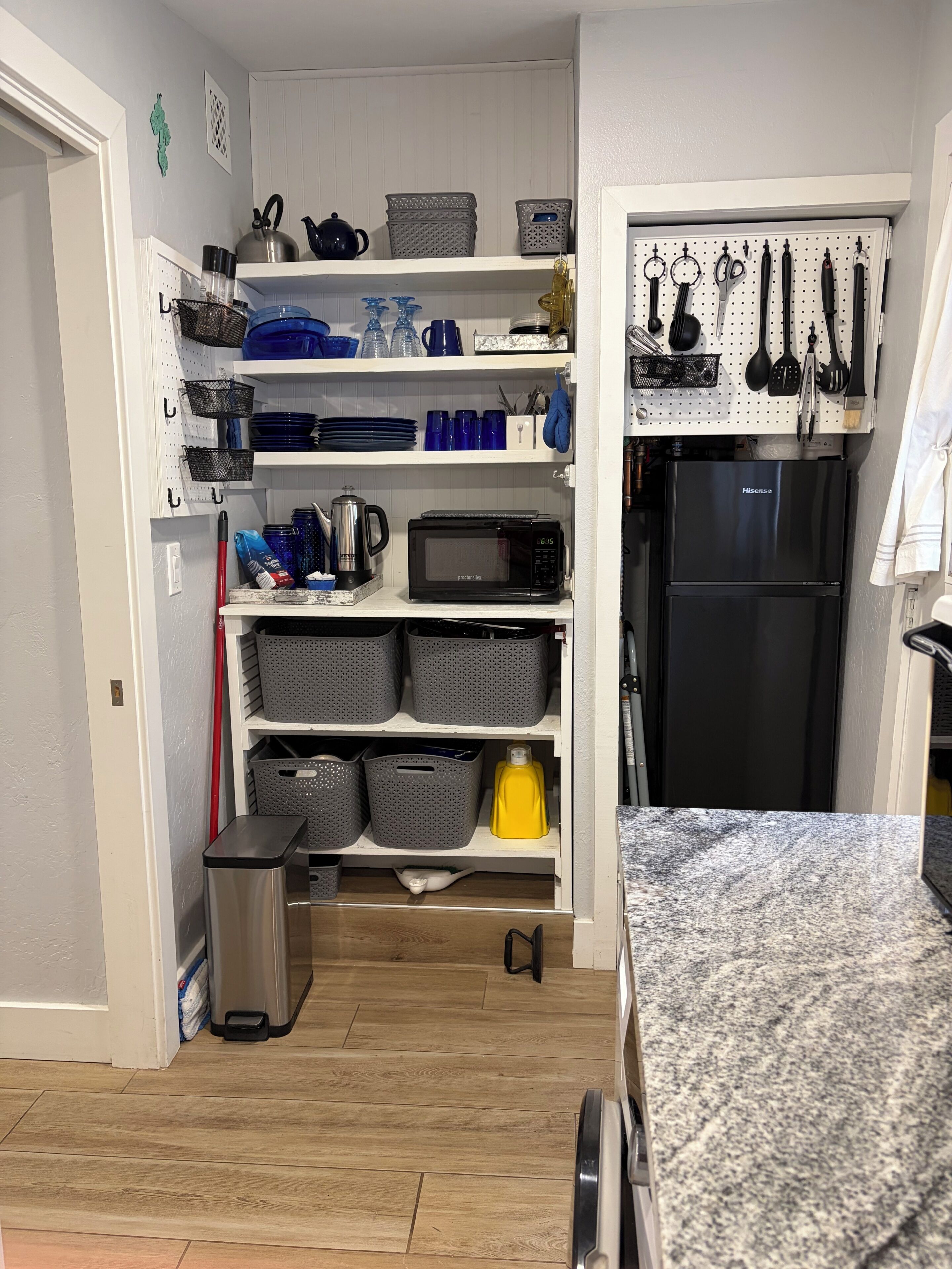 A kitchen with a microwave, shelves with kitchenware, and a refrigerator.