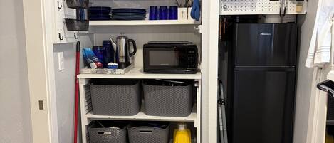 A kitchen with a microwave, shelves with kitchenware, and a refrigerator.