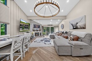 Een moderne woonkamer met een open haard, een eethoek en een groot raam met uitzicht op groen.