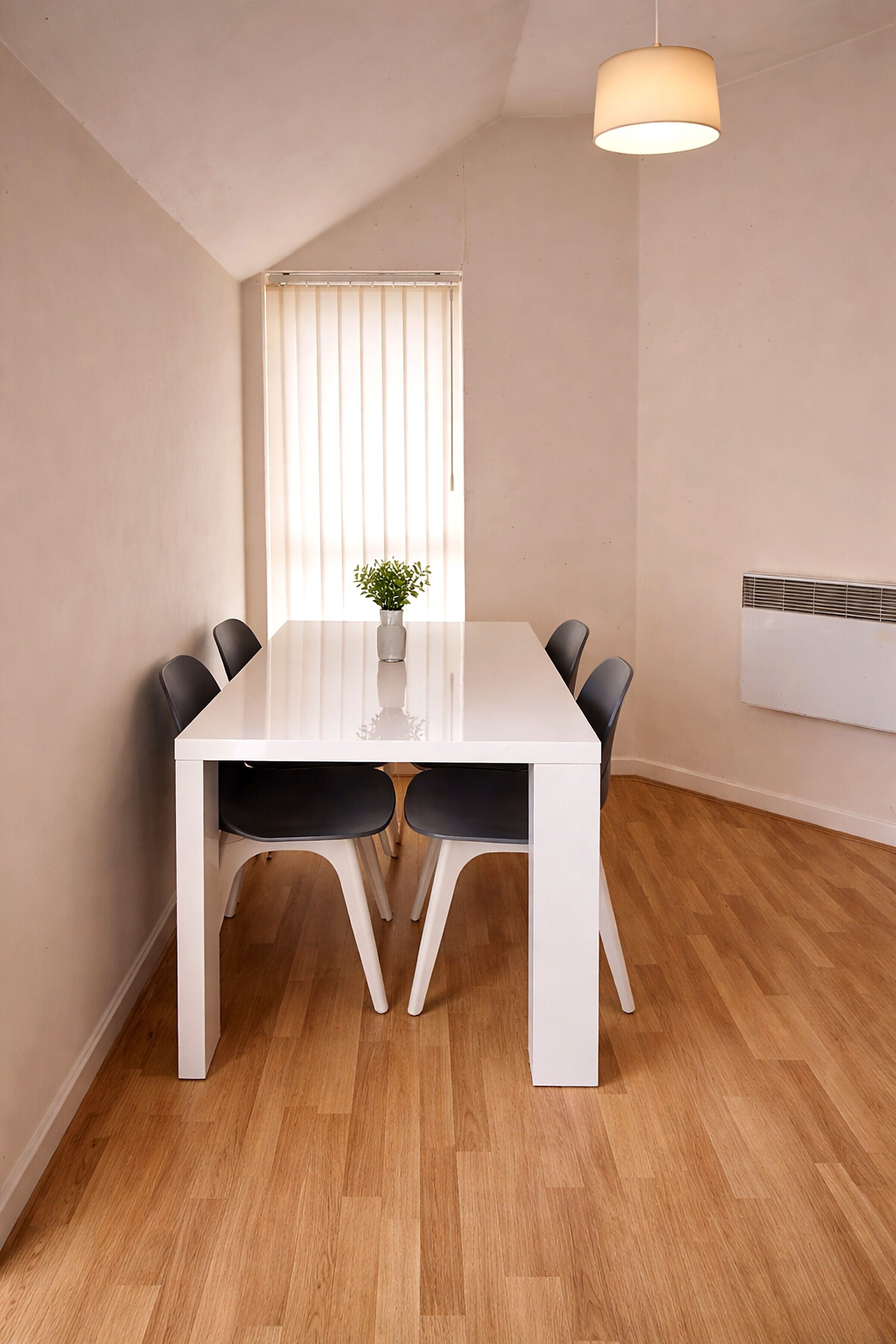 Une salle à manger moderne avec une table blanche, des chaises noires, une petite plante et un luminaire au plafond.