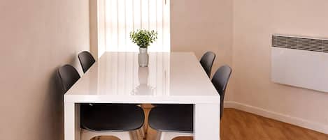 A modern dining room with a white table, black chairs, a small plant, and a ceiling light.