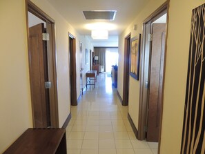 A hotel hallway with wooden doors, a tiled floor, and a dining area in the distance. - Spacious Dawn Beach 3-bedroom condo in delightful Upper Prince's Quarter (Upper Prince's Quarter)