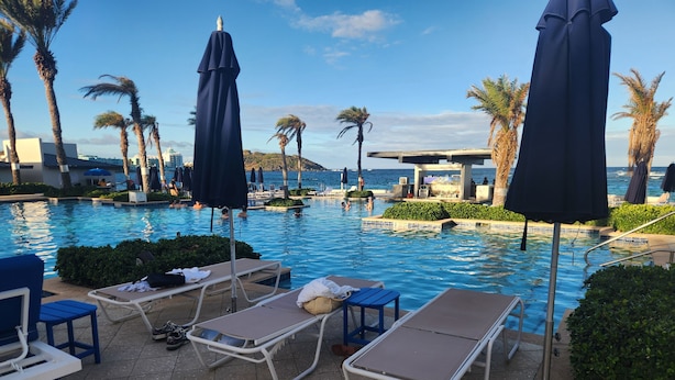 Ein Poolbereich mit Liegestühlen und Sonnenschirmen, einem gefliesten Boden und Blick aufs Meer.