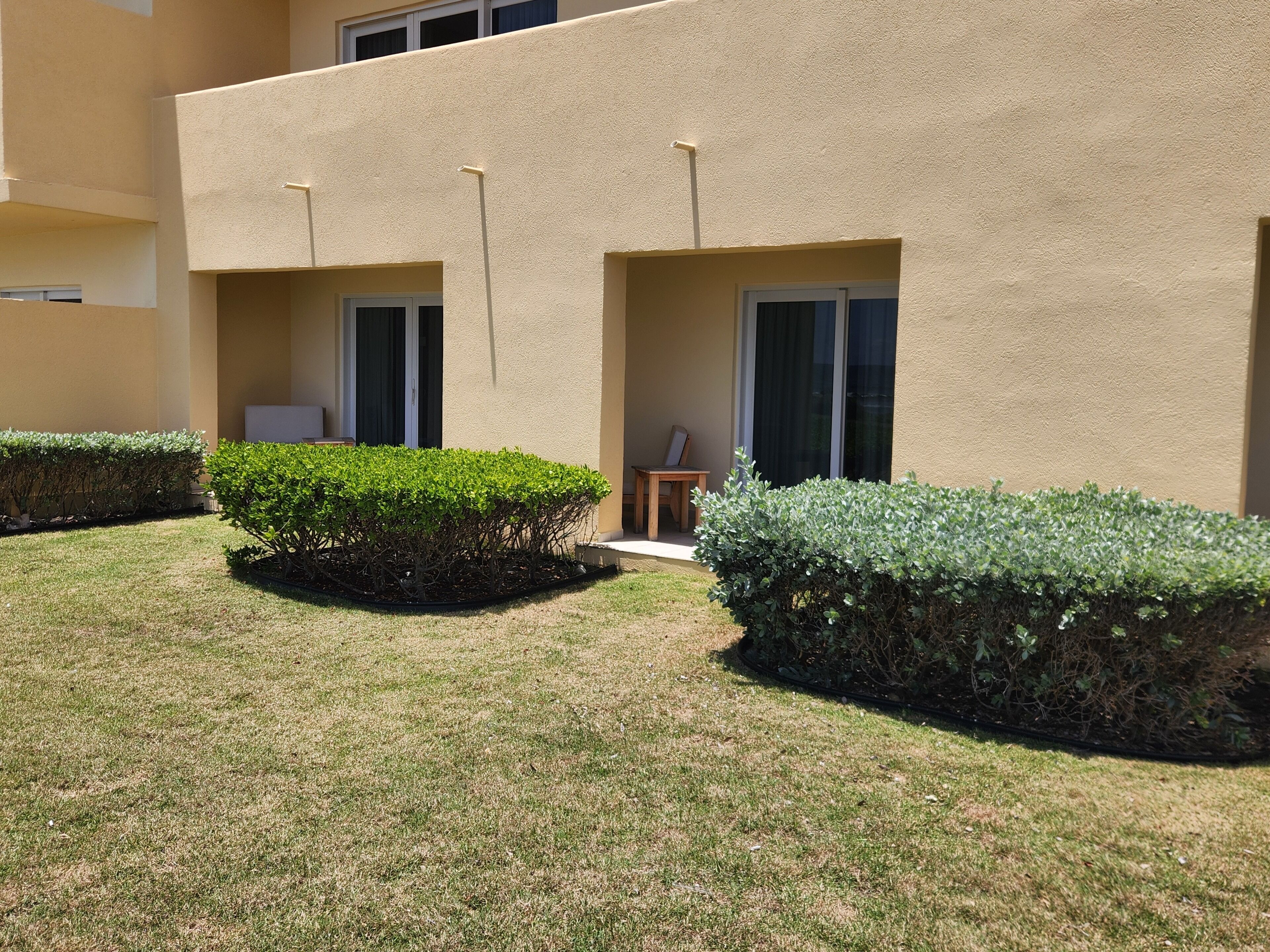 A building with a flat facade, two small windows, and a door. There is a well-maintained lawn with trimmed bushes.