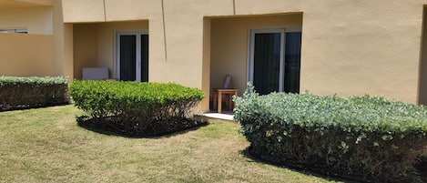 A building with a flat facade, two small windows, and a door. There is a well-maintained lawn with trimmed bushes.