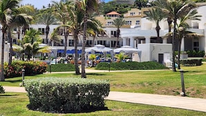 Ein Resort mit mehrstöckigen Gebäuden, Palmen und Sitzbereichen im Freien mit Sonnenschirmen.
