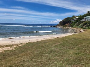 A coastal landscape with a sandy beach, grassy areas, and a rocky shoreline. - Spacious Dawn Beach 3-bedroom condo in delightful Upper Prince's Quarter (Upper Prince's Quarter)