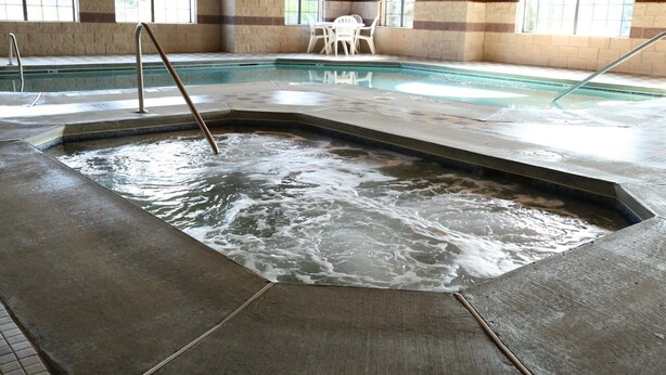 Una piscina interna con area idromassaggio, circondata da pareti in pietra e travi in legno.