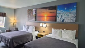 Una camera d'albergo con due letti, un comodino, una lampada e decorazioni murali raffiguranti scene naturali.