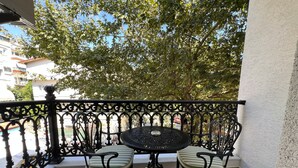 A balcony with a round table and two chairs, a wrought iron railing, and a view of trees and buildings. - Alâ Marmara Hotel (Marmara)