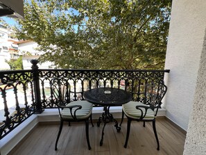 A balcony with a round table and two chairs, a wrought iron railing, and a view of trees and buildings. - Alâ Marmara Hotel (Marmara)