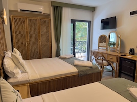 Habitación de hotel con cama, escritorio, silla, televisor y balcón con vista a zonas verdes.
