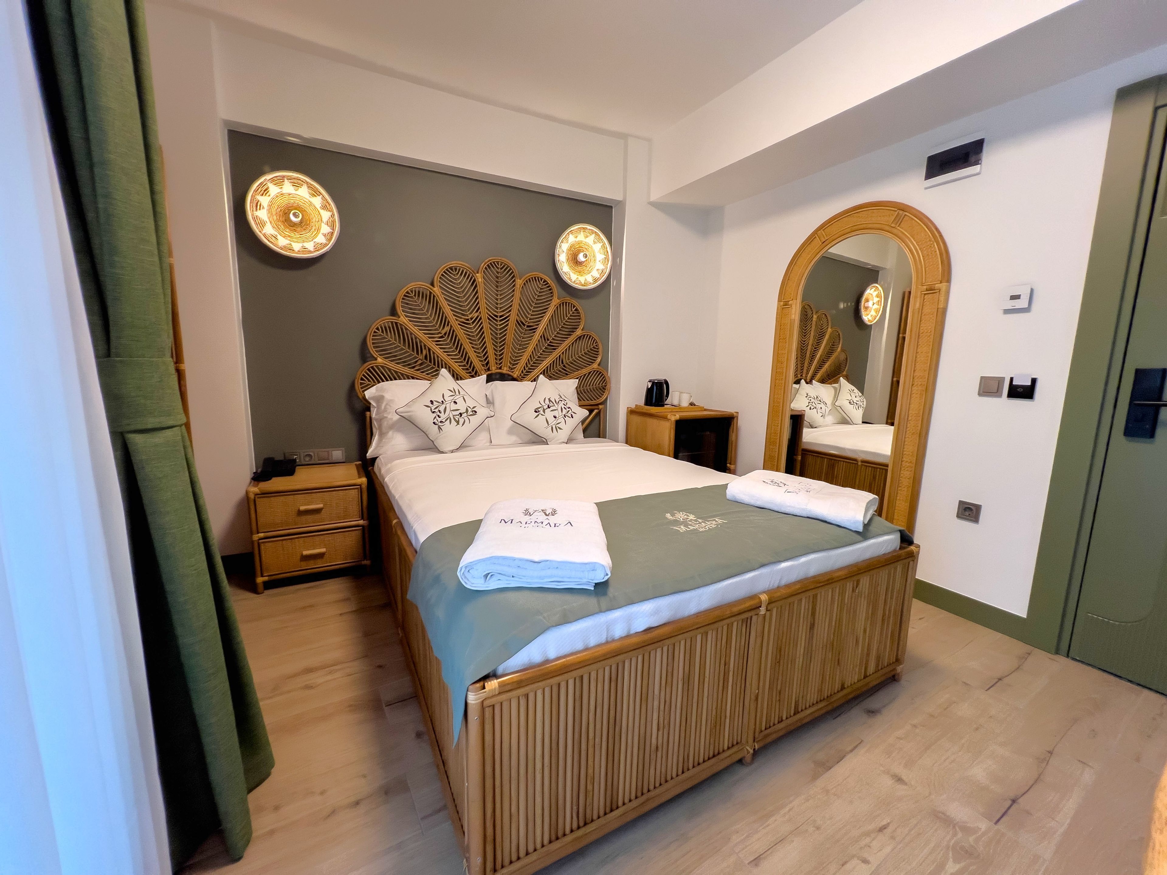 Een hotelkamer met een groot bed, een houten hoofdbord, een spiegel en een nachtkastje met een lamp.