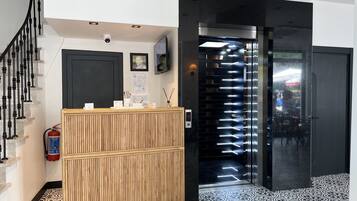 A reception area with a wooden counter, a fire extinguisher, a digital display, and a staircase.