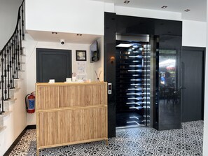 A reception area with a wooden counter, a fire extinguisher, a digital display, and a staircase.