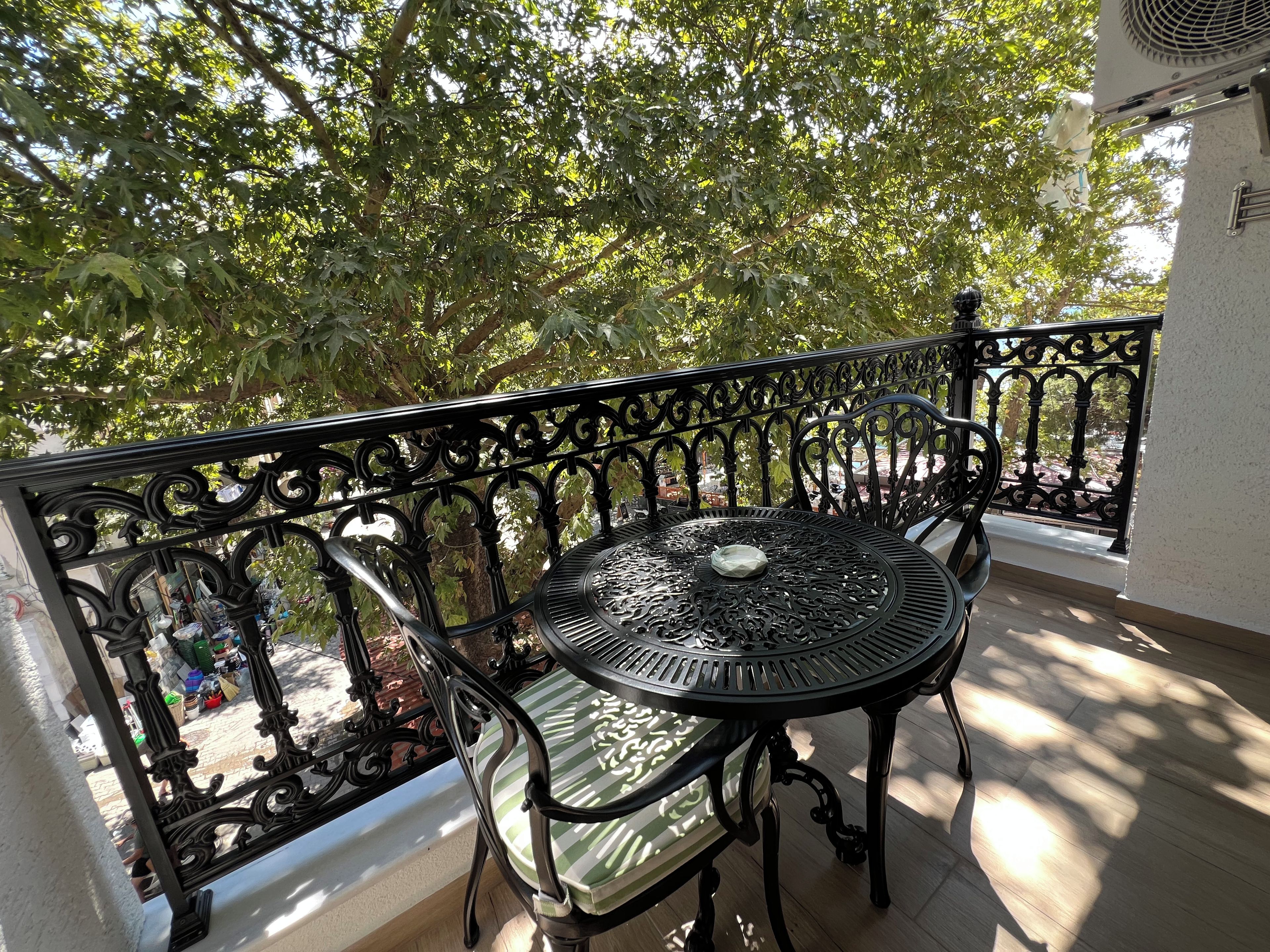 Ein Balkon mit einem Metalltisch und -stühlen, umgeben von einem schmiedeeisernen Geländer.