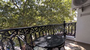 A balcony with a metal table and chair, surrounded by ornate black railings, and a view of trees and a building in the background. - Alâ Marmara Hotel (Marmara)