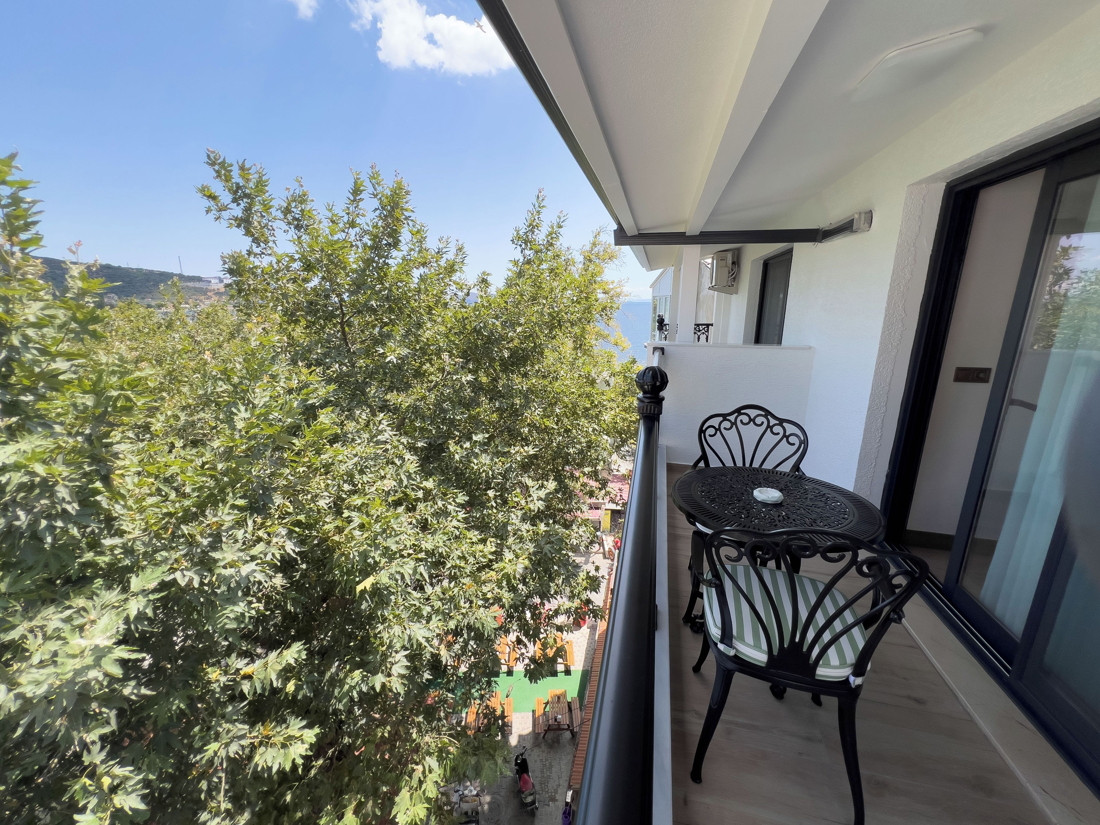 Ein Balkon mit Tisch und Stühlen, der auf eine Straße mit abgestellten Rollern und einem Baum blickt.