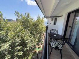 Ein Balkon mit Tisch und Stühlen, der auf eine Straße mit abgestellten Rollern und einem Baum blickt.