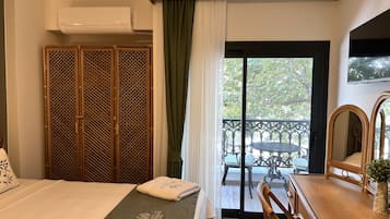 A hotel room with a bed, a wooden wardrobe, a balcony with a table and chairs, and a television mounted on the wall.