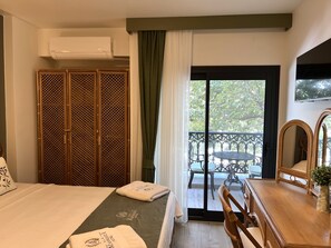 Habitación de hotel con cama, armario de madera, balcón con mesa y sillas, y televisor montado en la pared.