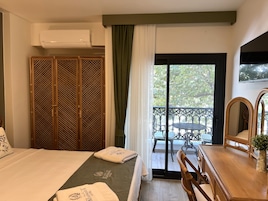 Habitación de hotel con cama, armario de madera, balcón con mesa y sillas, y televisor montado en la pared.