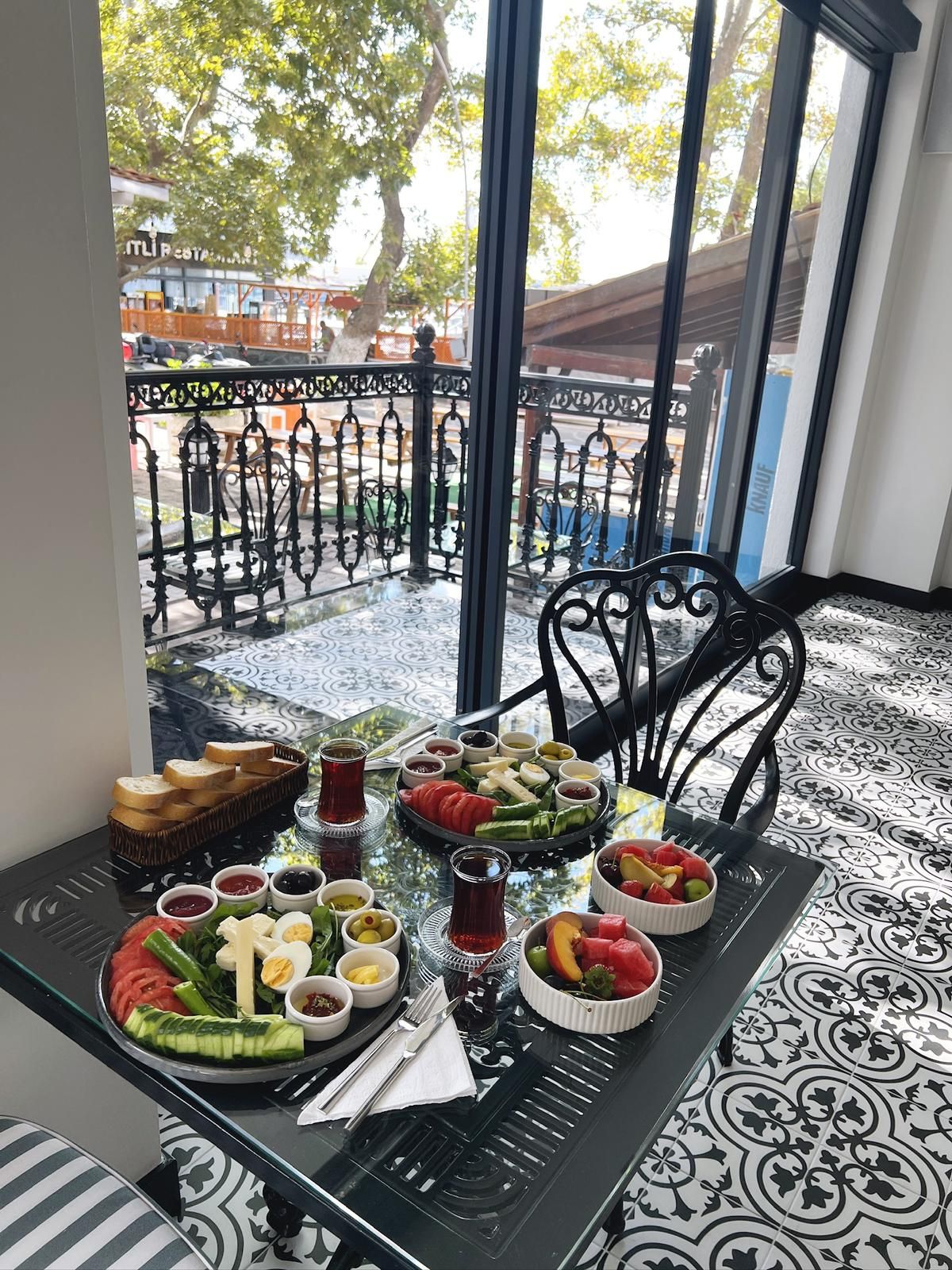 Una mesa de comedor con diversos alimentos y bebidas, sobre un suelo estampado, con vistas a un balcón y zona de estar al aire libre.