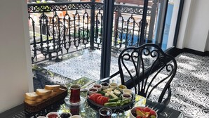 Una mesa de comedor con diversos alimentos y bebidas, sobre un suelo estampado, con vistas a un balcón y zona de estar al aire libre.