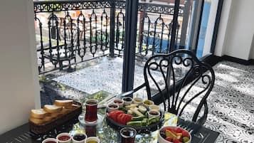 Una mesa de comedor con diversos alimentos y bebidas, sobre un suelo estampado, con vistas a un balcón y zona de estar al aire libre.