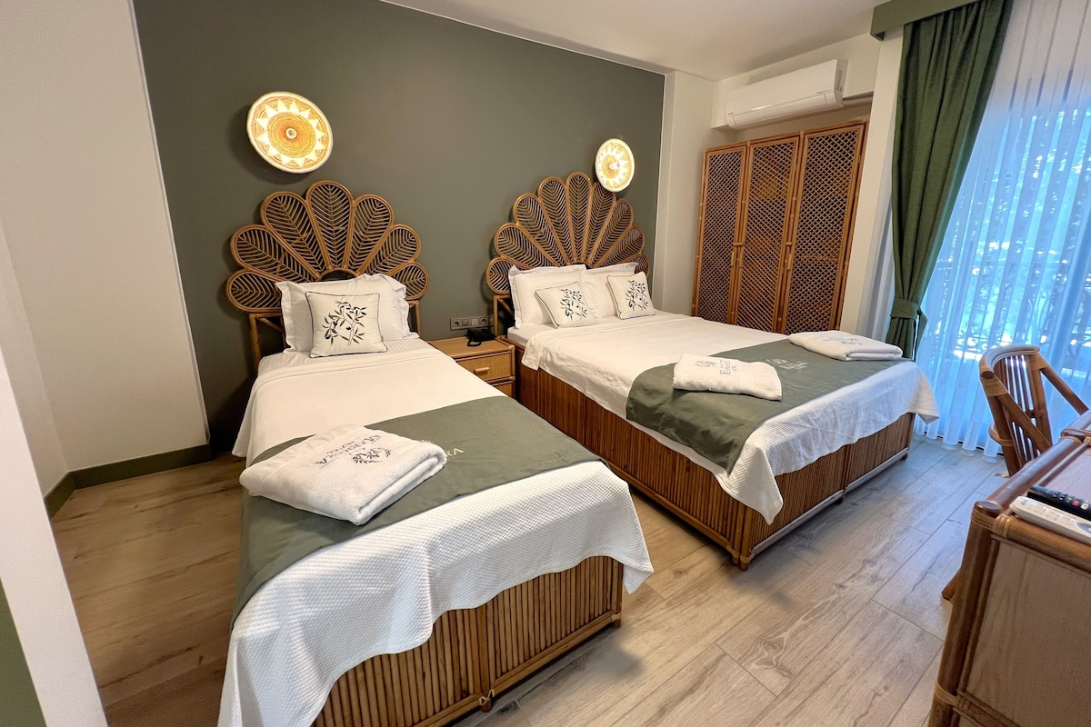 A hotel room with two beds, wooden headboards, a nightstand, and a view of the outdoors.