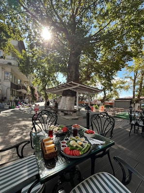 An outdoor dining area with a table set for a meal, surrounded by trees and a building in the background.